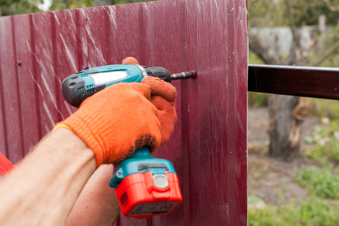 Metal fence installation. Work man in gloves with a drill