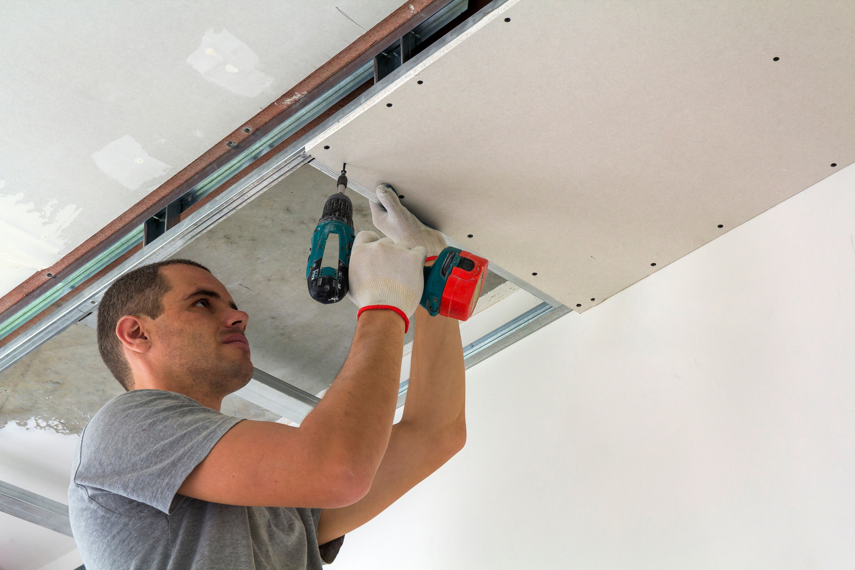 Construction worker assemble a suspended ceiling with drywall and fixing the drywall to the ceiling metal frame with screwdriver.