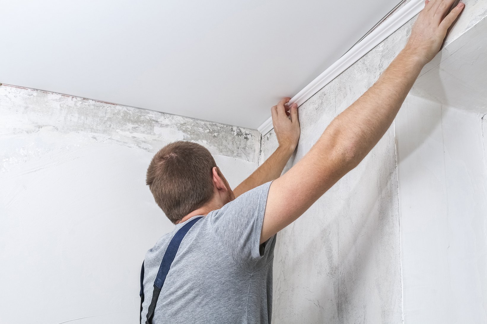 Worker Fixes the Plastic Molding to Ceiling. Installation of Ceiling Cornice.